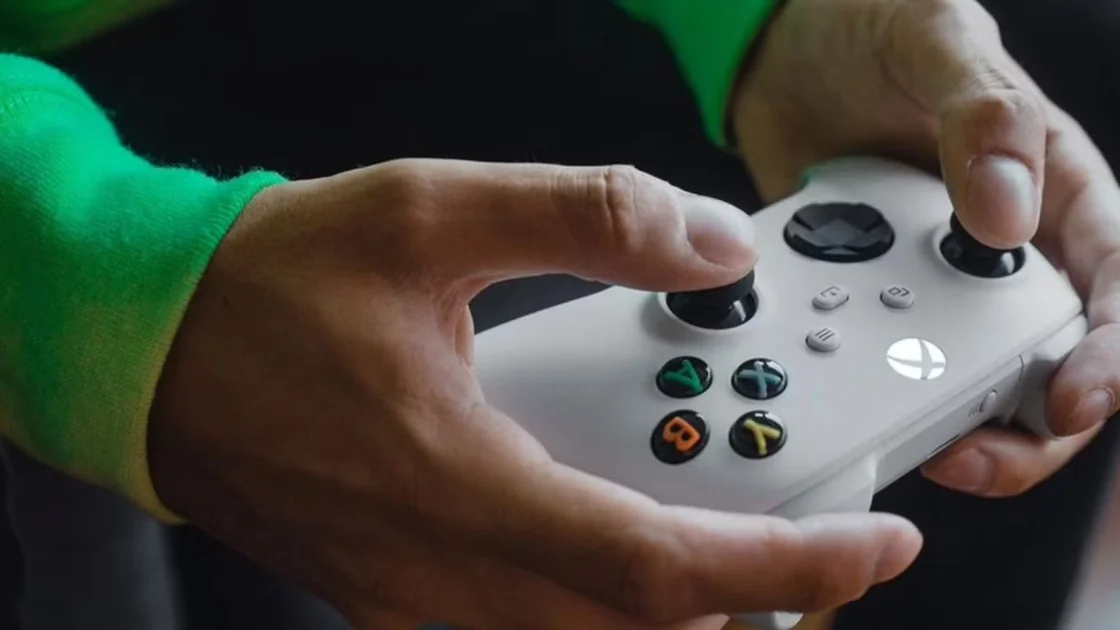 Close up of a white Xbox controller behind held by someone in a green top