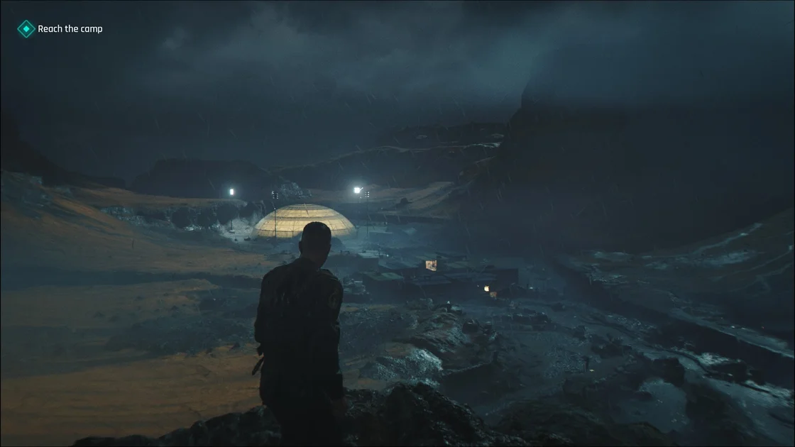 A screenshot of 007 First Light, showing Bond in Iceland overlooking an enemy encampment at night. A large, illuminated dome structure sits at the end of the camp.