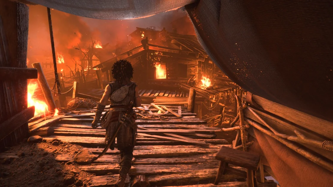 Resonance: A Plague Tale Legacy screenshot showing a traditional video game over-the-shoulder shot of player character Sophia advancing towards a series of wooden cabins that are aflame
