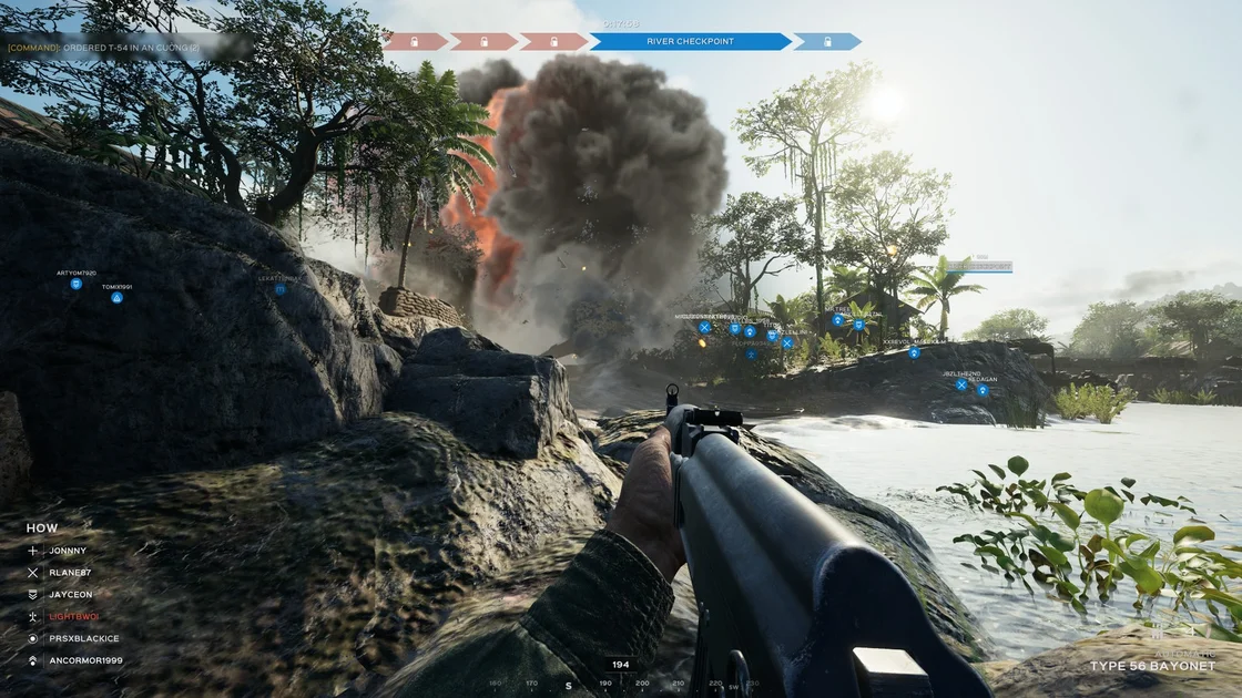 A Screenshot of Hell Let Loose: Vietnam, showing the player lying on some rocks beside a river, as a bomb detonates a few yards in front of him.
